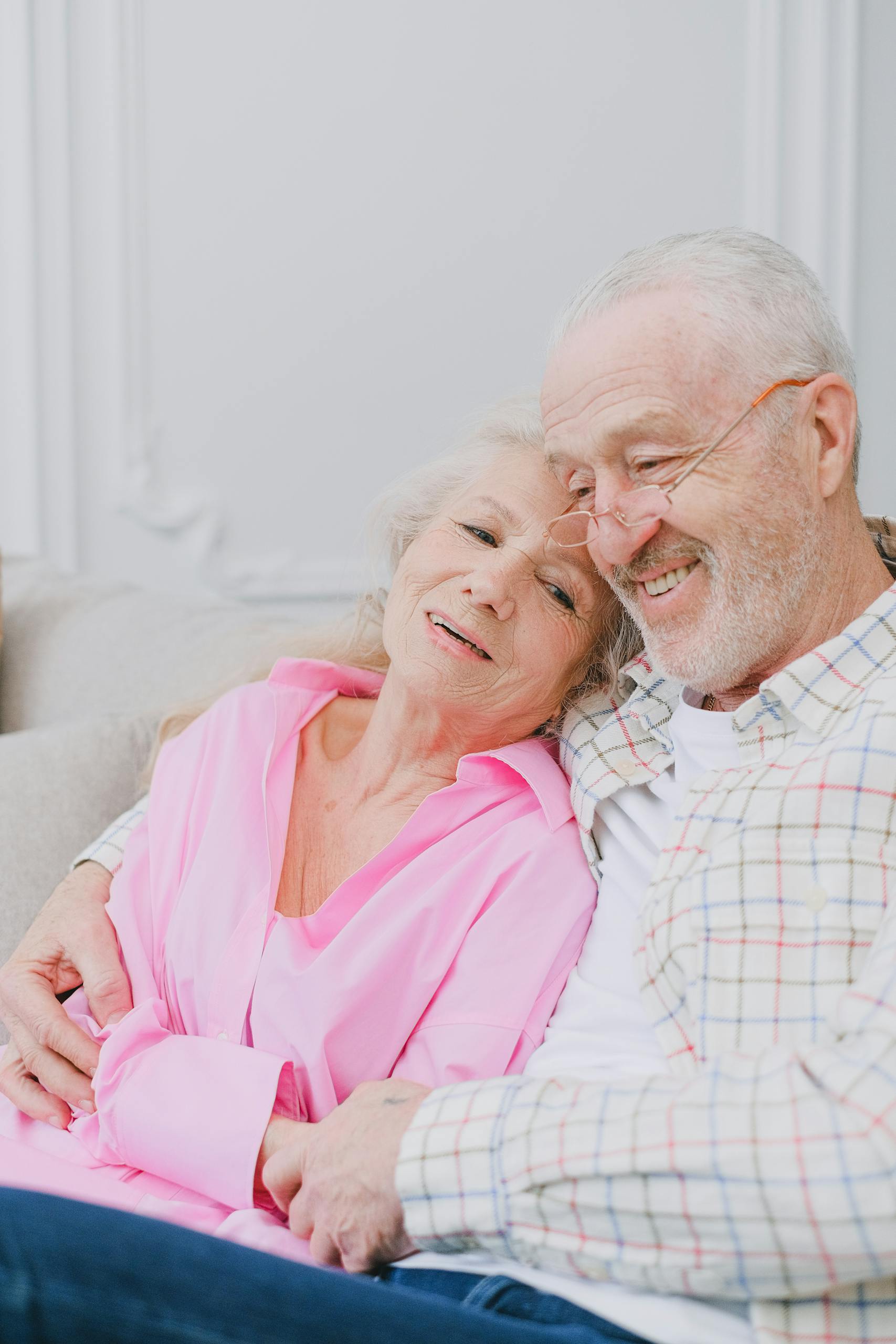 Elderly couple sitting together, smiling warmly and displaying affection indoors.