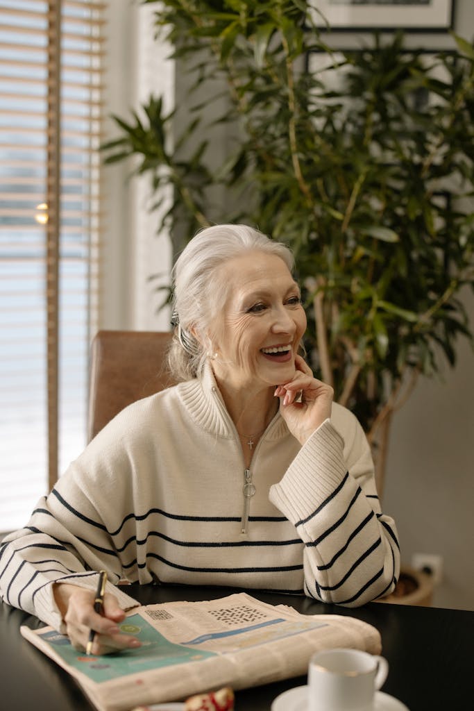 Smiling elderly woman solving crossword puzzle at home, enjoying a quiet indoor moment.