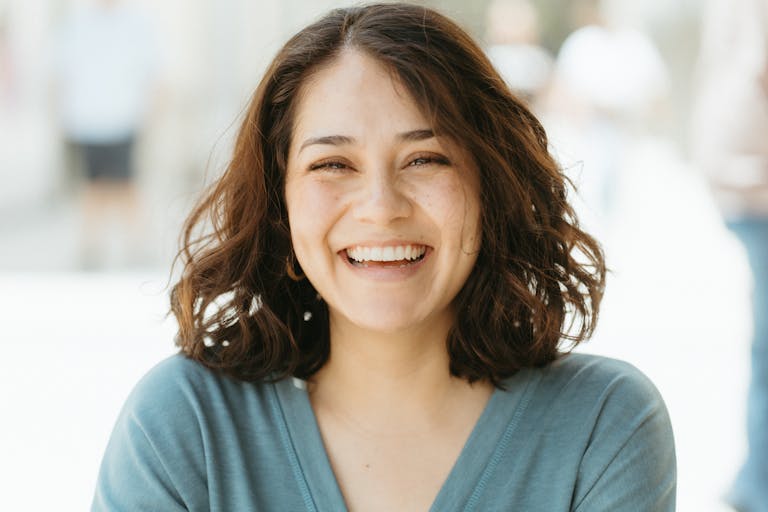 A joyful woman smiling broadly against a sunlit outdoors background. Warm and inviting photo.