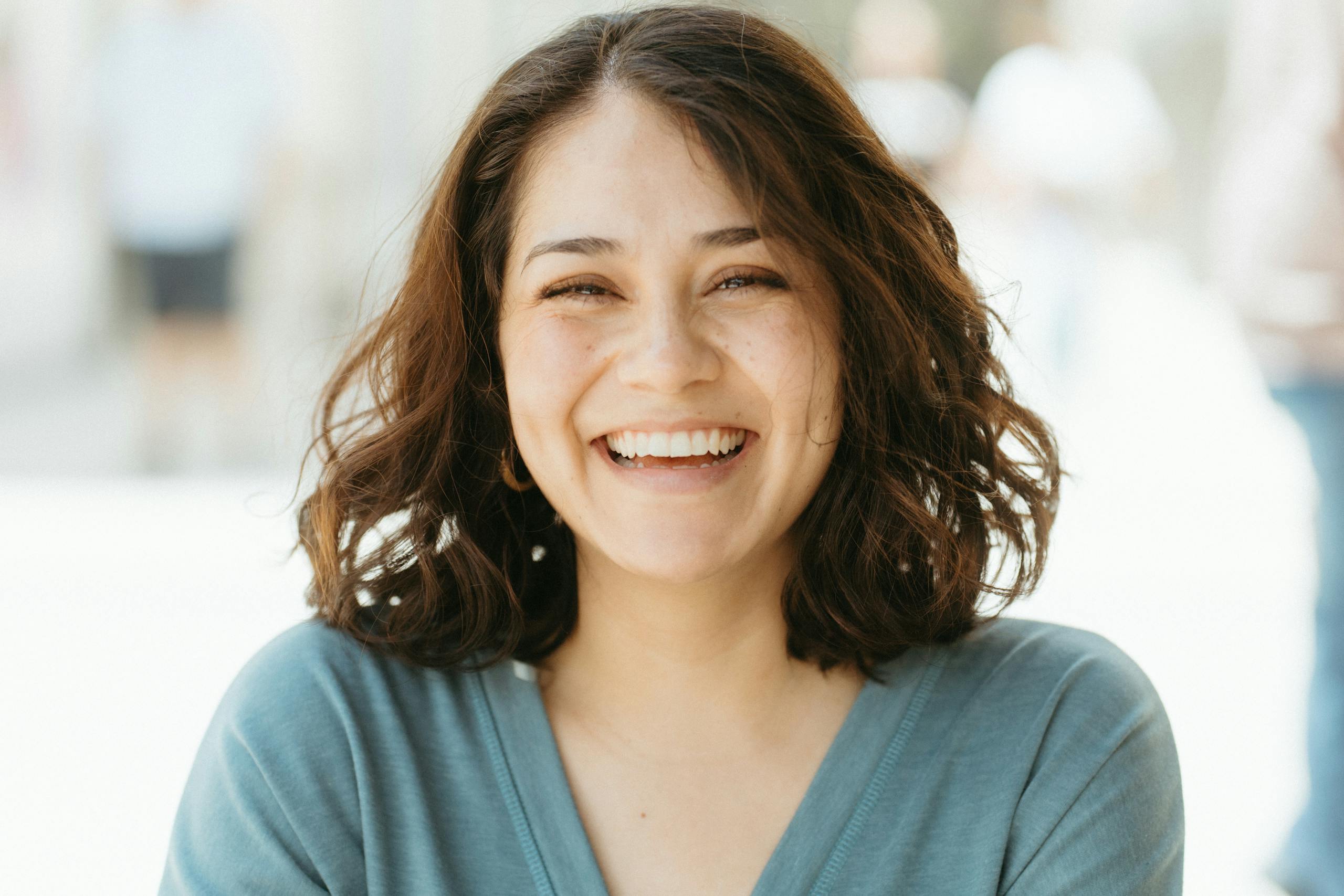 A joyful woman smiling broadly against a sunlit outdoors background. Warm and inviting photo.
