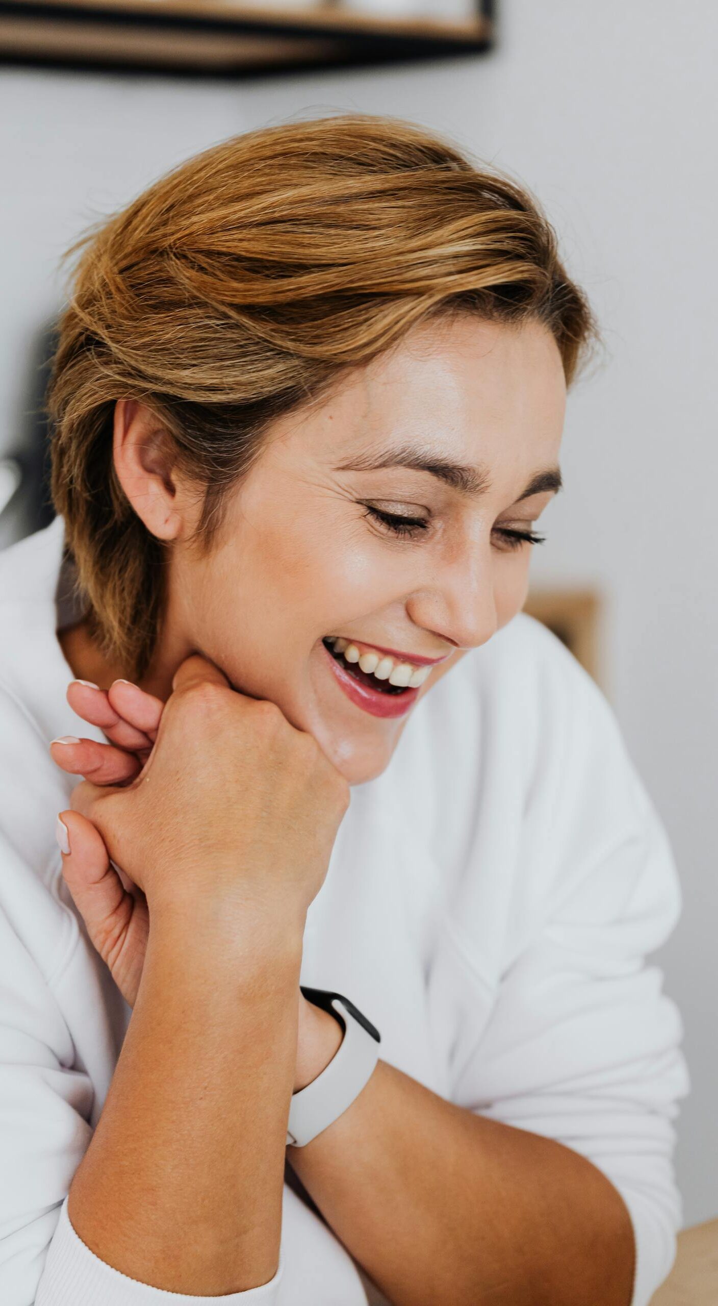 A joyful woman with short hair laughing indoors, showing warmth and positivity.