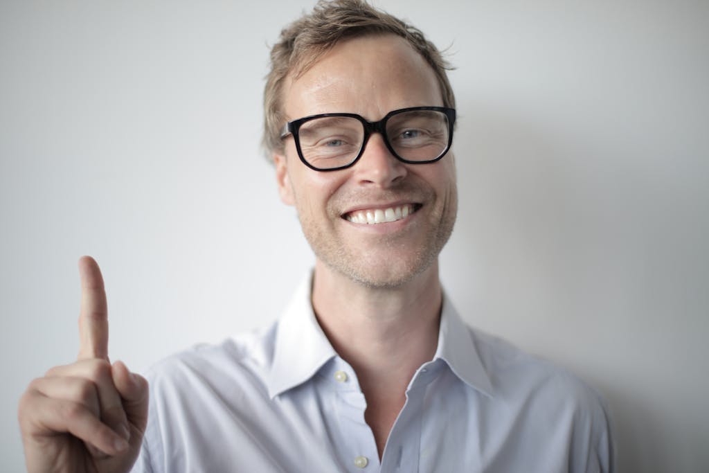 Portrait of a happy man wearing glasses and a white shirt, gesturing with his hand.